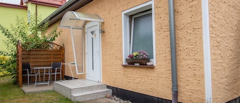 A house with a small patio, a door, a window with a flower box, and a visible gutter.