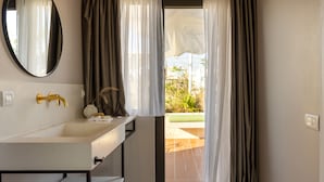 A bathroom with a white sink, gold faucet, and a mirror. There is a door leading to an outdoor area with a view of greenery. - L'Avventura Athens (Athens)