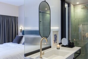 A modern hotel room with a large bed, a bathroom with a glass shower enclosure, and a vanity with a mirror. - L'Avventura Athens (Athens)