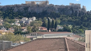 A person reading a magazine on a balcony with a view of ancient ruins and a cityscape. - L'Avventura Athens (Athens)