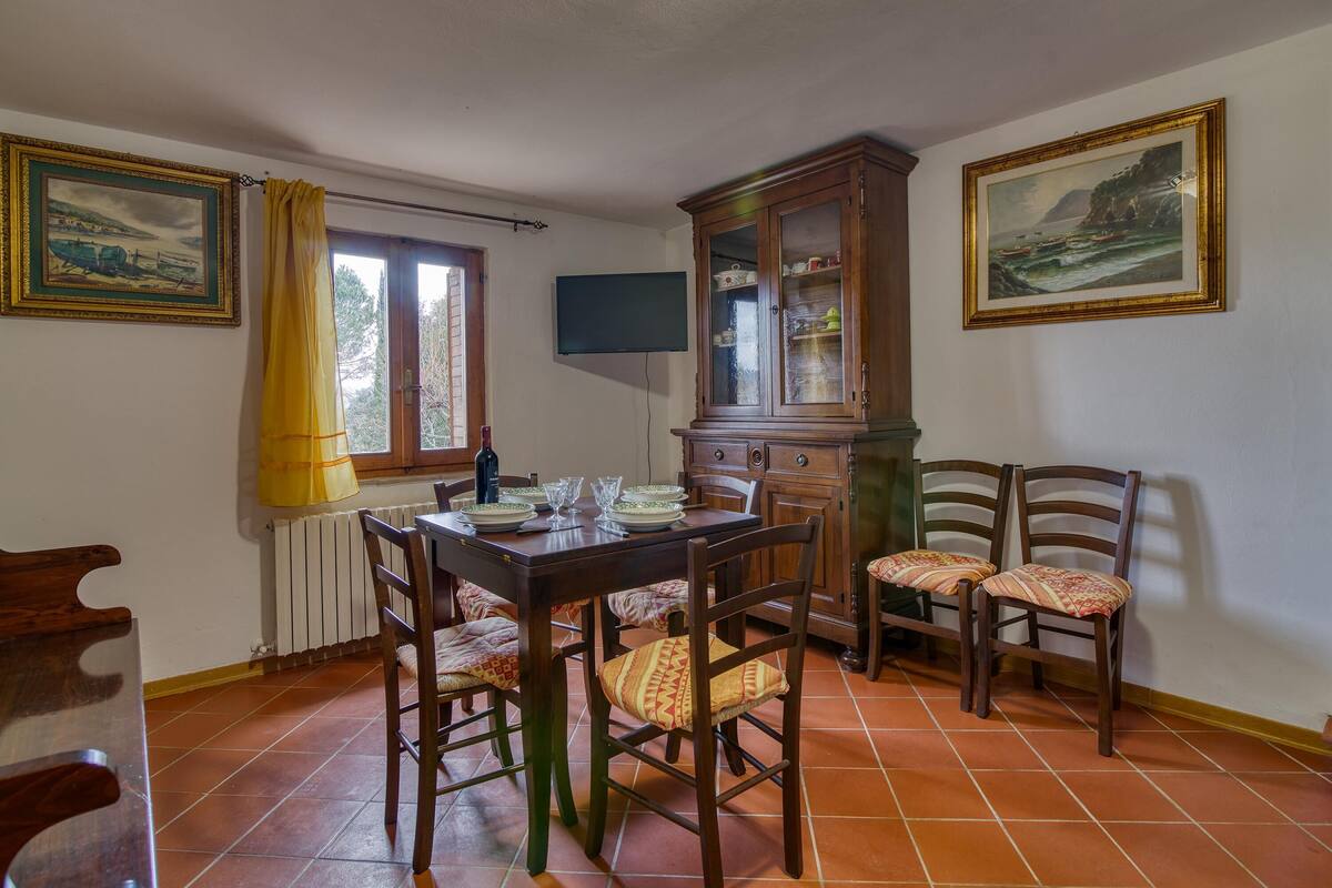 A dining area with a wooden table, chairs, a cabinet, and two paintings on the walls.