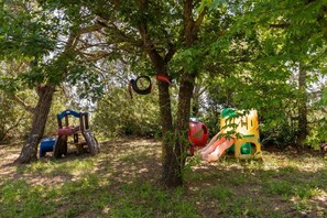 Ein Spielplatz mit Rutschen und Schaukeln, umgeben von Bäumen.