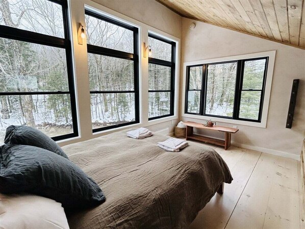 A bedroom with a large bed, two windows, a bedside table, and a bench.