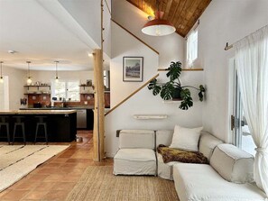 A modern kitchen with a central island, a dining area with a sofa, and a staircase leading to an upper level.
