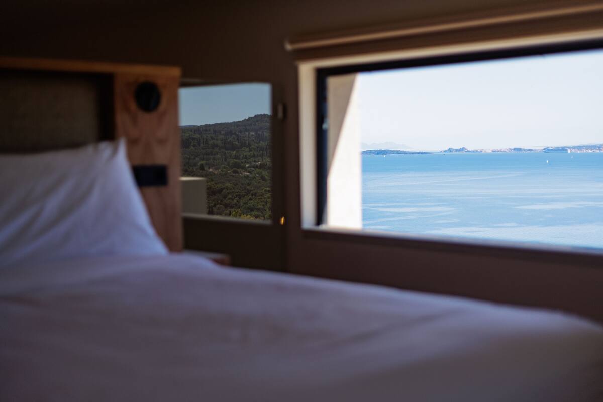 A bed with a headboard and a window with a view of a body of water and distant land.