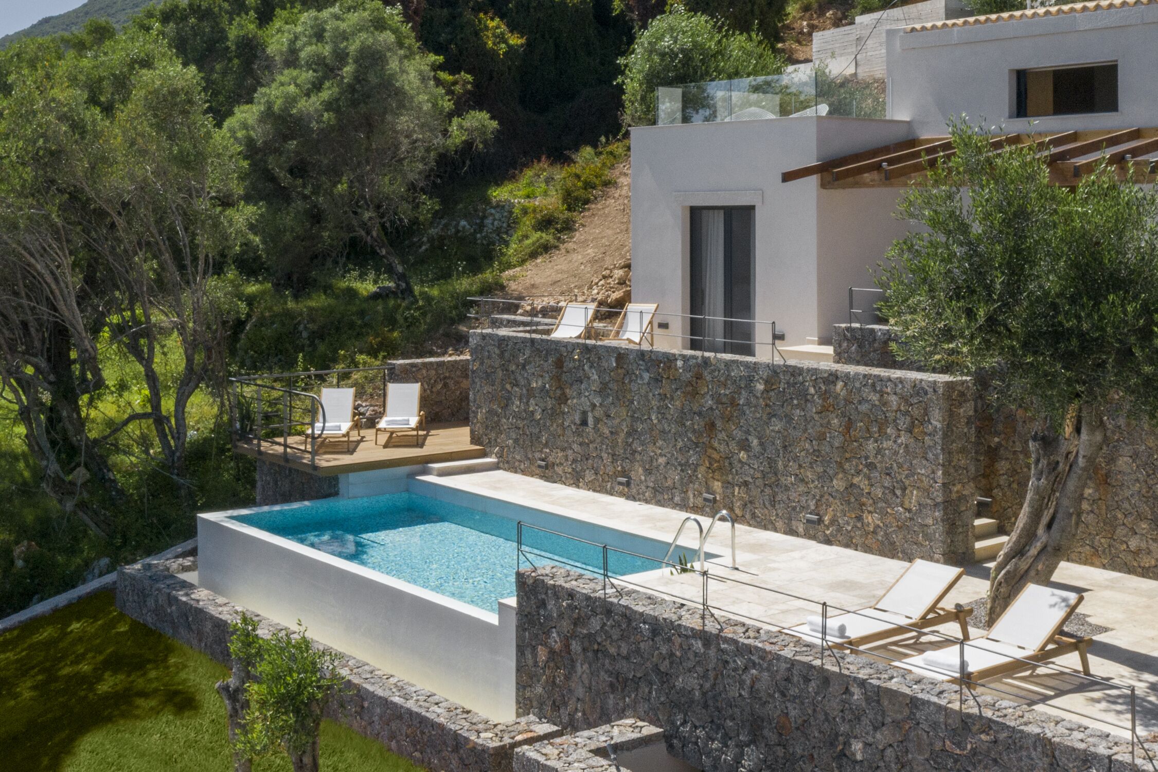 Un área de piscina moderna con una pared de piedra, sillas de descanso y una piscina azul cristalina.