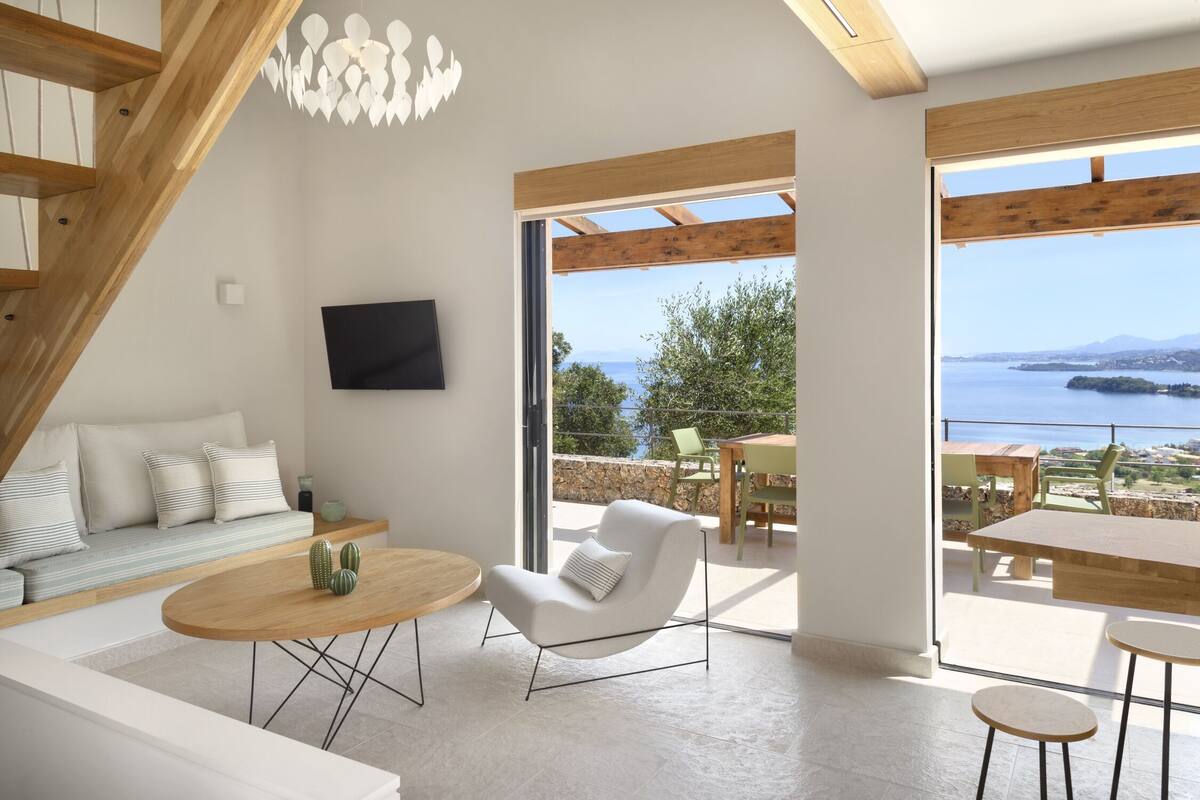 A modern living room with a sofa, a round coffee table, and a chair, with a view of the sea and a balcony.