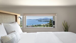 A bedroom with a large bed, a window with a view of a lake and mountains, and a plant on the windowsill. - Greenstone Villas (Corfu)