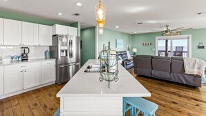 A modern kitchen with white cabinets, a stainless steel refrigerator, and a central island. - Beachfront | Expansive Deck, Grill & Ocean Views (Gilchrist)