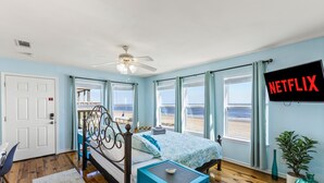 A bedroom with a bed, a TV, and a view of the beach. - Beachfront | Expansive Deck, Grill & Ocean Views (Gilchrist)