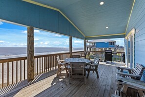 A wooden deck with a table and chairs, overlooking a beach. - Beachfront  | Expansive Deck, Grill & Ocean Views (Gilchrist)