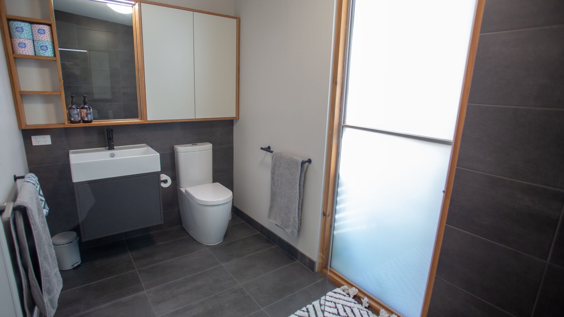 A modern bathroom with a white sink, toilet, and a towel hanging on the wall.