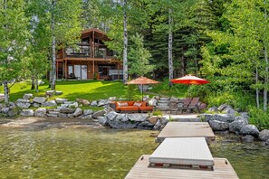 A lakeside cabin with a deck, outdoor seating, and a clear view of the surrounding forest. - McCall Lakefront Oasis - Family Summer Paradise - Hot tub - Dock - 4 Bedrooms (McCall)