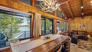 Un interior de madera con una mesa de comedor, sillas, un sofá y un ventanal con vistas a un lago.