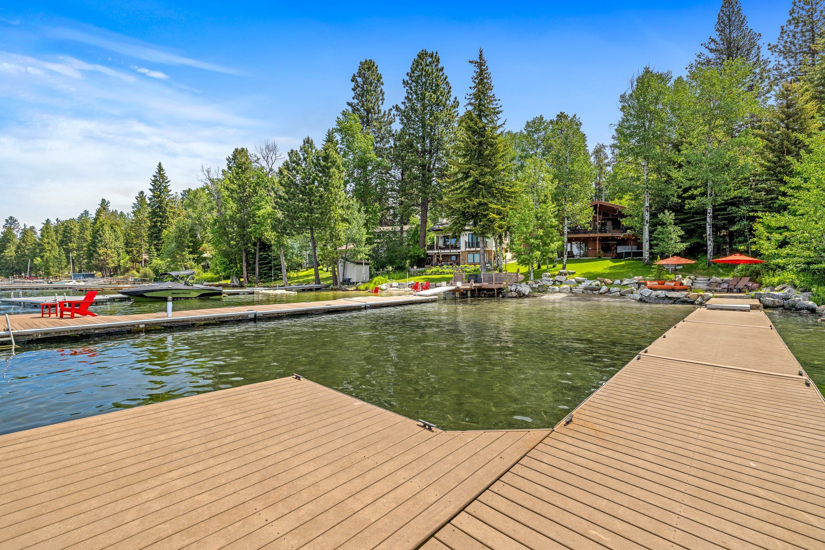 A wooden dock leading to a calm lake with a house in the background surrounded by trees.