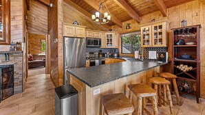 Una cocina amplia con armarios de madera, una isla grande con taburetes, electrodomésticos de acero inoxidable y una araña.