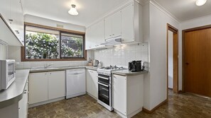 A modern kitchen with white cabinets, a built-in oven, and a window overlooking a garden.