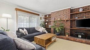 A living room with a brick fireplace, a grey sofa, a wooden coffee table, and a flat-screen TV mounted on the wall.