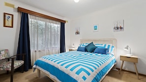 A bedroom with a bed, a chair, a nightstand, and a window with curtains.