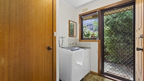 A laundry room with a washing machine, a sink, and a window with a view of greenery.