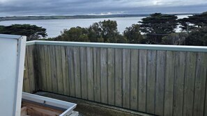 Une vue depuis un balcon doté d’une balustrade en bois, donnant sur une étendue d’eau et sur une terre lointaine.