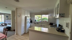 A compact kitchen with white cabinets, a built-in oven, and a window providing natural light. - Dune Retreat - Point Lonsdale (POINT LONSDALE)