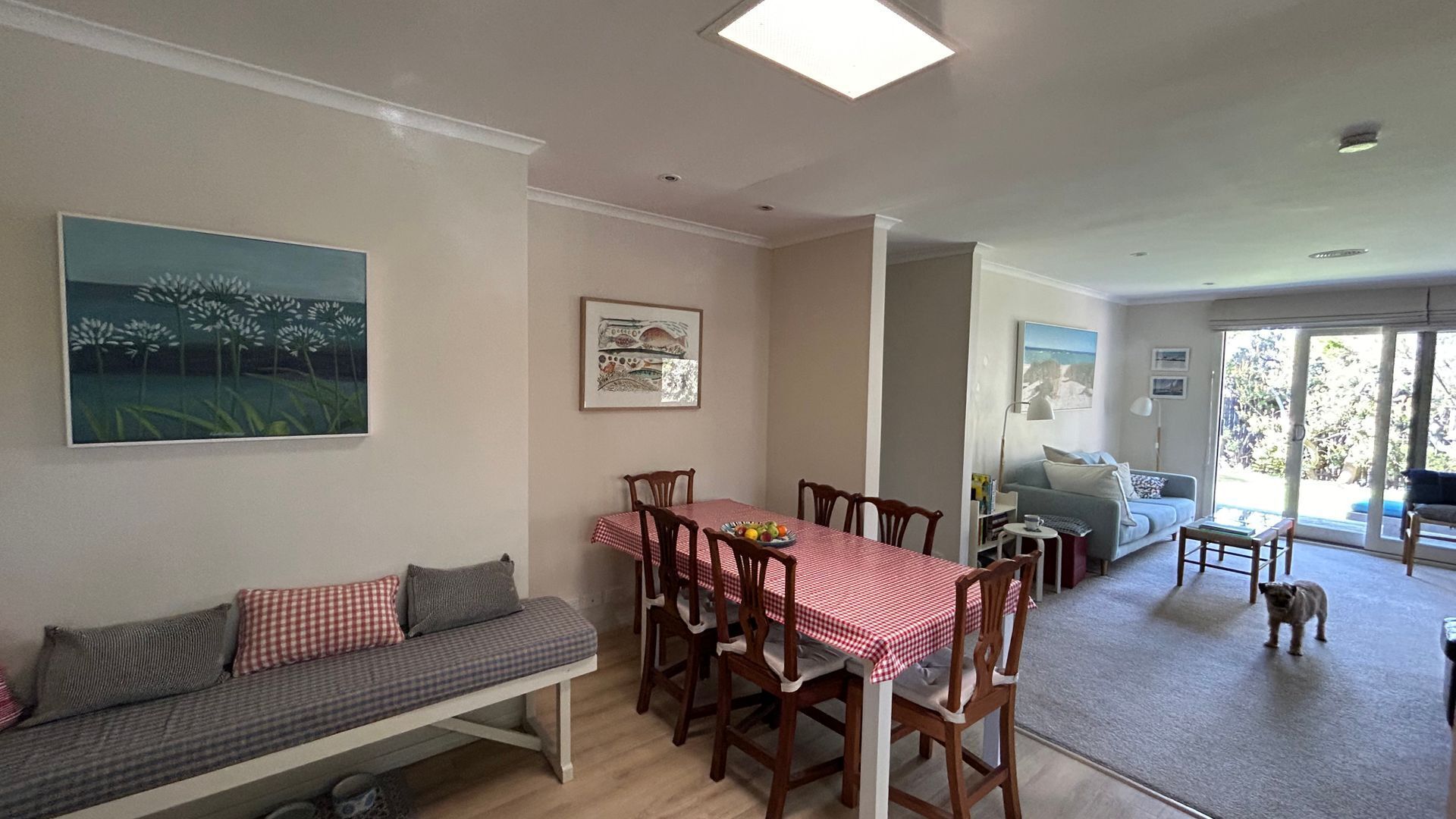 Een eethoek met een tafel voor vier personen, een bank met kussens, en een schilderij aan de muur.