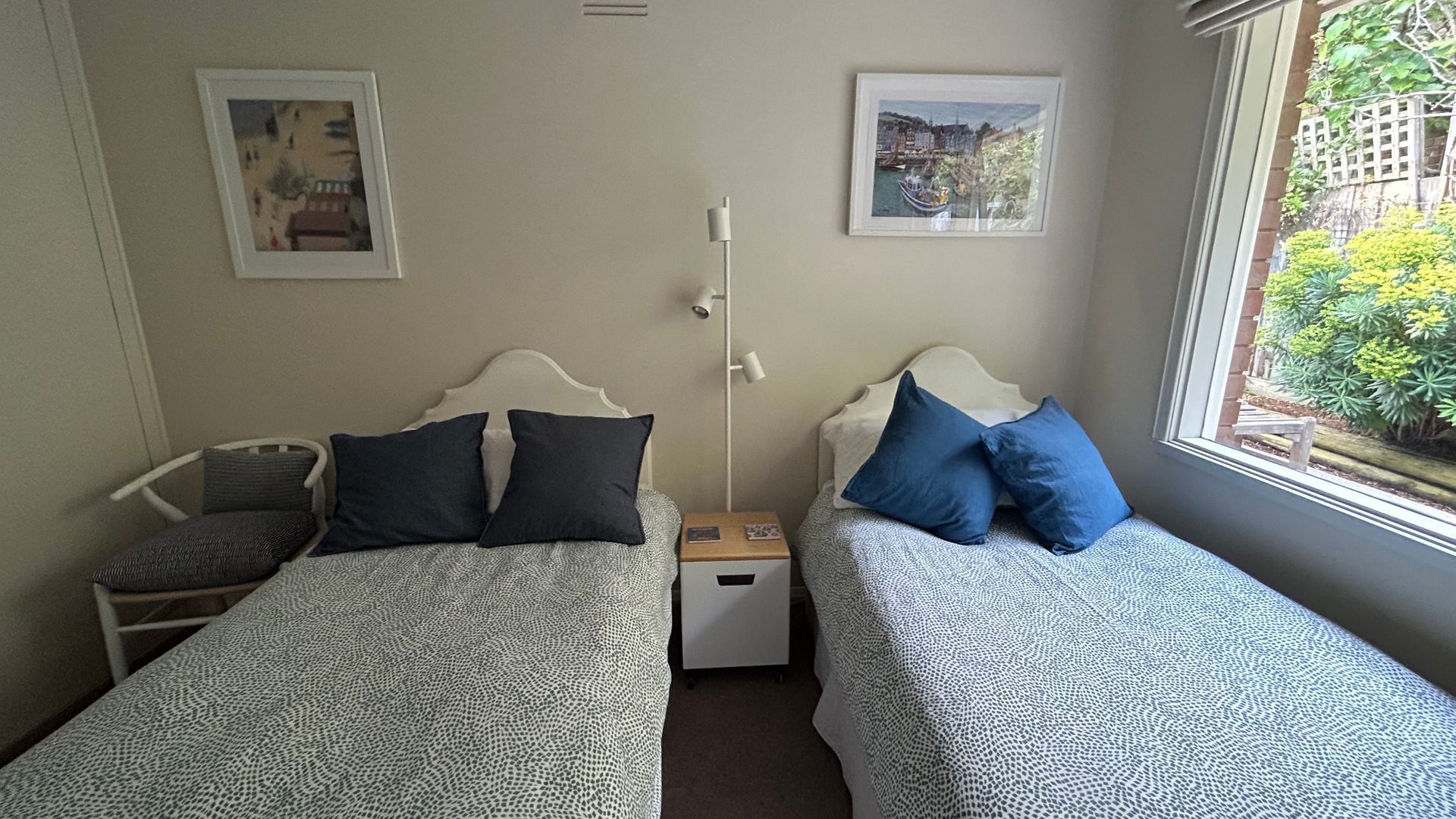 A bedroom with two beds, a nightstand, a chair, and two framed pictures on the wall.