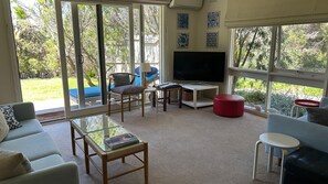 A living room with a TV, seating, and large windows. - Dune Retreat - Point Lonsdale (POINT LONSDALE)