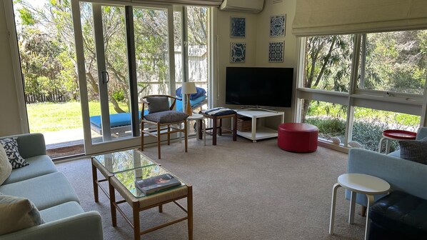 A living room with a TV, seating, and large windows. - Dune Retreat - Point Lonsdale (POINT LONSDALE)