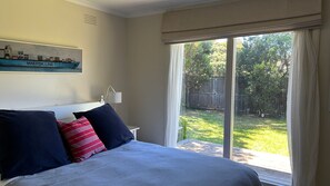 A bedroom with a bed, a nightstand, a lamp, and a window with a view of a backyard.