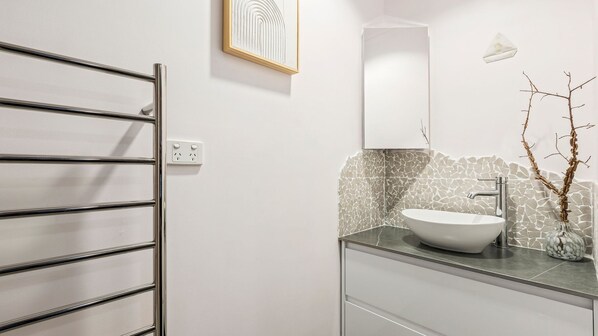 A modern bathroom with a freestanding bathtub, a large mirror, and a stone mosaic backsplash.