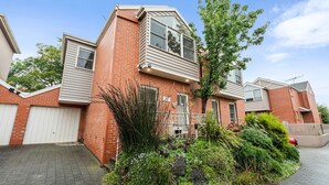 Un immeuble résidentiel à la façade en briques, doté de nombreuses fenêtres et agrémenté d’un jardin bien entretenu où poussent diverses plantes et arbustes.