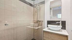A modern bathroom with a glass-enclosed shower, a white sink, and a mirror above the sink.