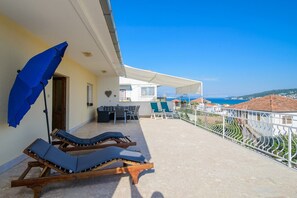 Un balcón con sillones de sol y una mesa, con vistas a la costa.