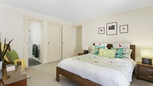 A bedroom with a bed, bedside tables, a nightstand, a mirror, and a door leading to a bathroom. - Private Hideaway - Point Lonsdale (POINT LONSDALE)