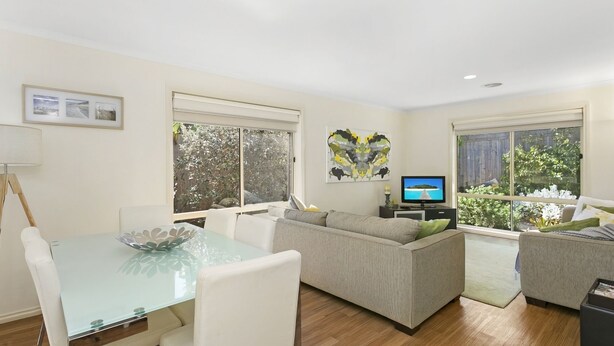 A modern living room with a glass dining table, two sofas, and a TV. - Private Hideaway - Point Lonsdale (POINT LONSDALE)