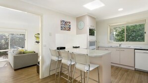 A modern kitchen with a central island, bar stools, a built-in oven, and a window with a view of greenery. - Private Hideaway - Point Lonsdale (POINT LONSDALE)