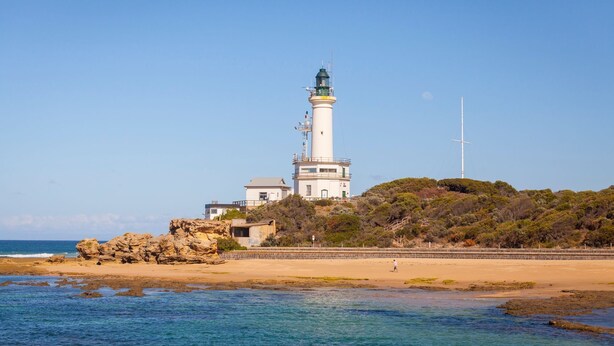 A lighthouse on a rocky outcrop with a clear view of the sea and a person walking on the beach. - The 20th Hole - Point Lonsdale (POINT LONSDALE)