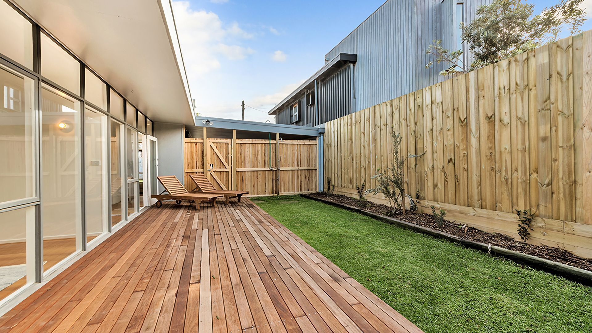 A modern outdoor patio with wooden flooring and a small lawn area.
