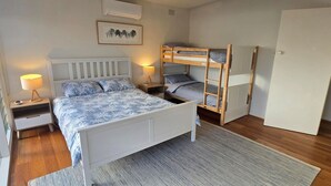 A bedroom with a single bed, a bunk bed, a bedside table with a lamp, a nightstand, a framed picture on the wall, and a door. - The 20th Hole - Point Lonsdale (POINT LONSDALE)