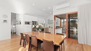 A modern kitchen with white cabinets, a wooden dining table, and a view of the outdoors through a sliding glass door.