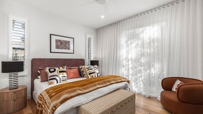 A modern bedroom with a bed, bedside tables, a chair, and a large window with curtains.
