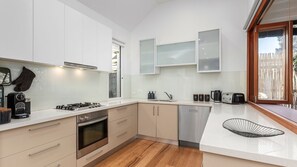 A modern kitchen with white cabinets, a stainless steel oven, a dishwasher, and a large window.