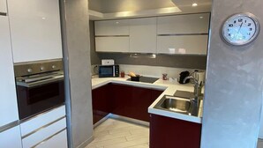 A modern kitchen with white cabinets, a built-in oven, a microwave, a sink, and a clock on the wall. - Romantica Suite modern apartment in Verbania Intra (Verbania)