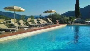 Piscina con sillas de descanso y sombrillas, rodeada de montañas.