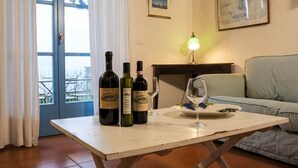 Una habitación con una mesa que sostiene botellas de vino y copas, un sofá, una lámpara y una puerta que da al exterior.