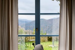A room with a large window, a view of a mountainous landscape, and a balcony with a chair.