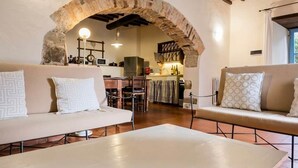 A cozy living area with a stone archway, a sofa, a coffee table, and a kitchen in the background.