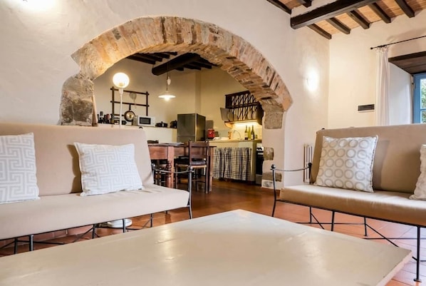 A cozy living area with a stone archway, a sofa, a coffee table, and a kitchen in the background.